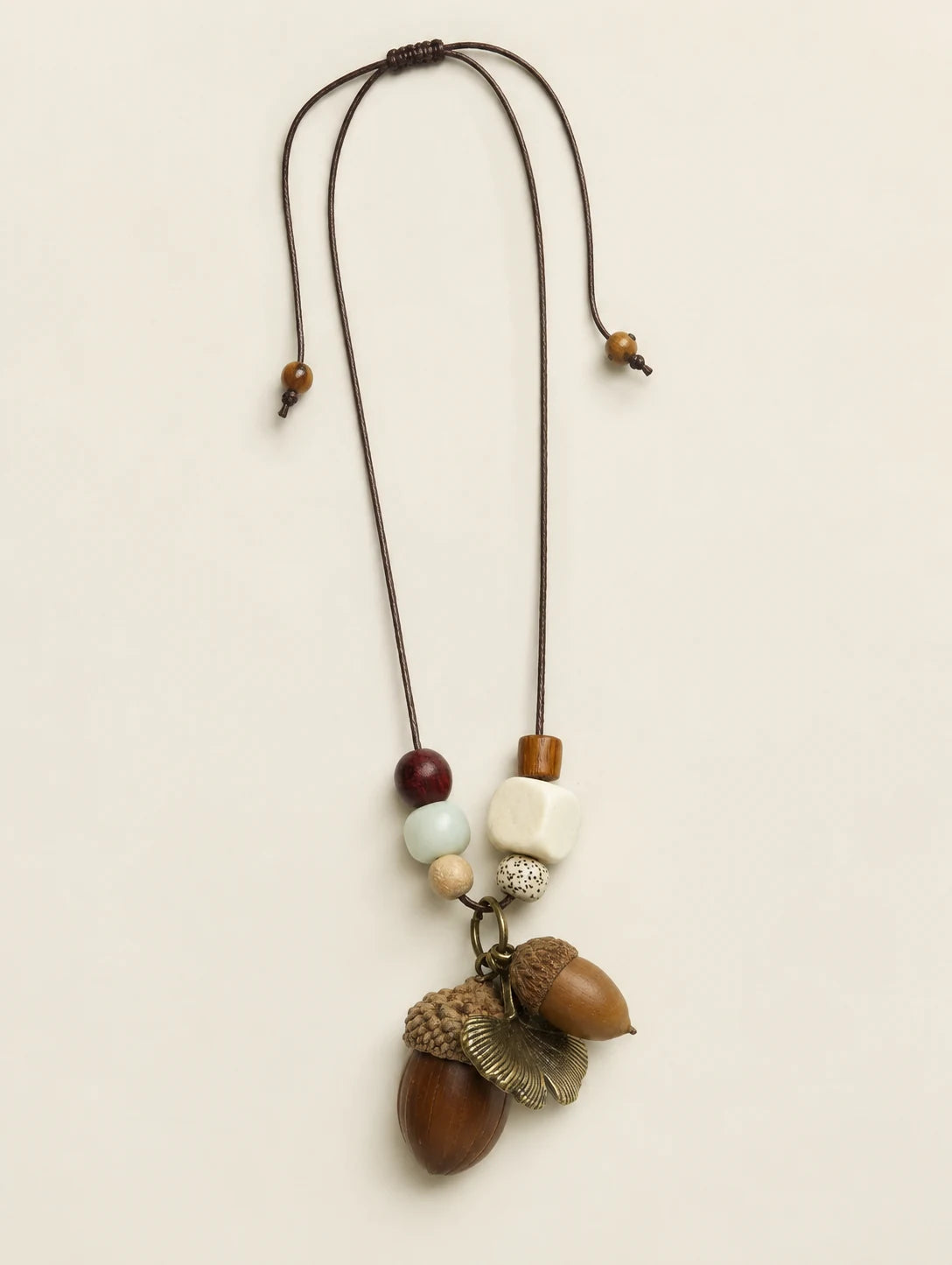 Brown Acorn-Silhouette Necklace — complete product view on a warm ivory background