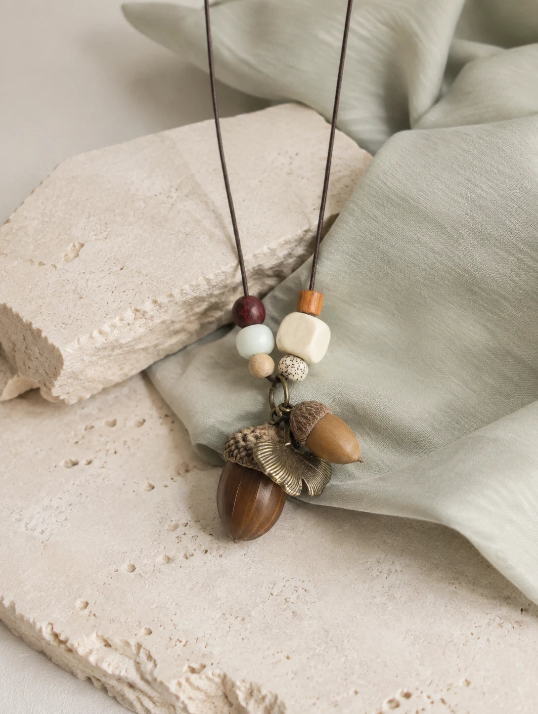 Brown Acorn-Silhouette Necklace — restrained editorial still life