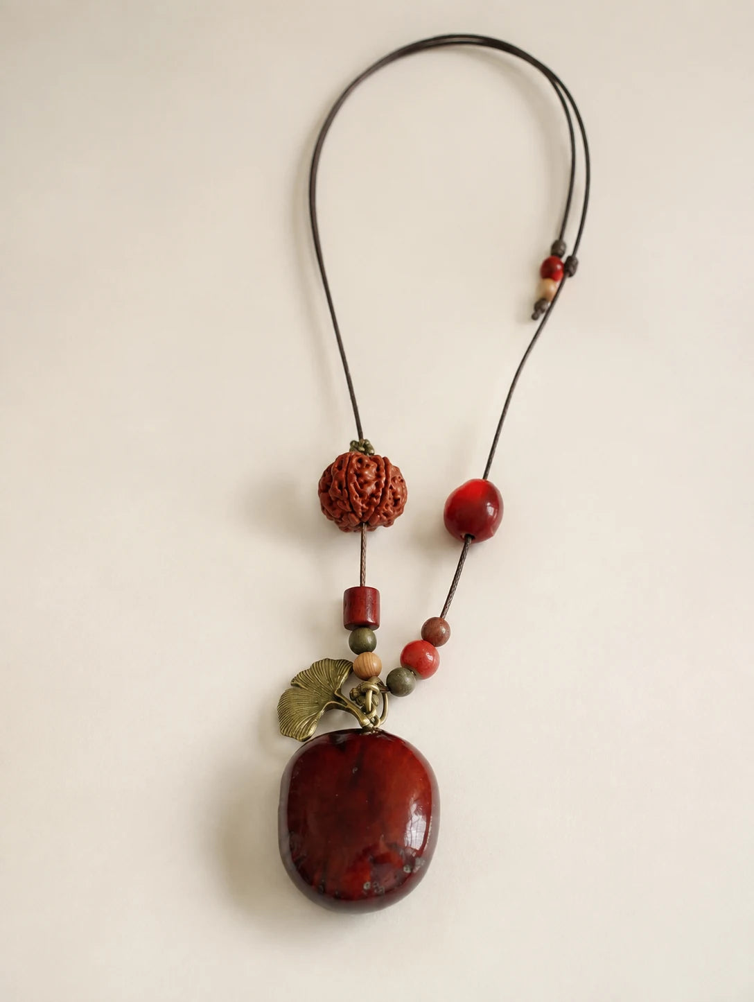 Deep Red Seed Pendant Necklace — complete product view on a warm ivory background