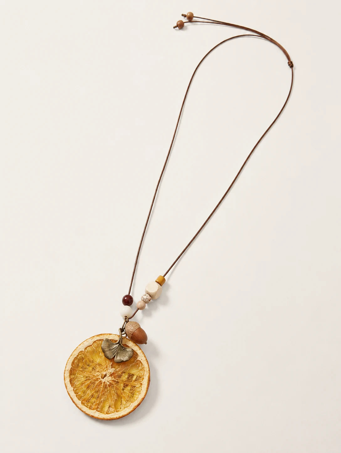 Orange Disc and Acorn Necklace — complete product view on a warm ivory background