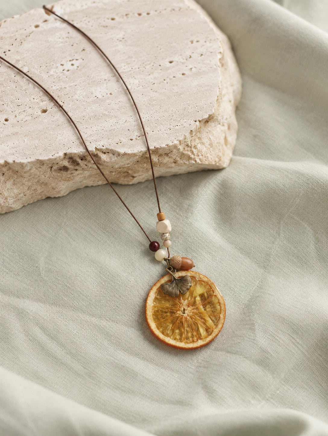 Orange Disc and Acorn Necklace — restrained editorial still life